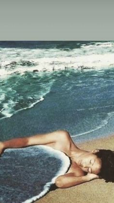 a woman laying on top of a sandy beach next to the ocean