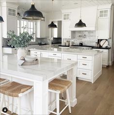 a large kitchen with white cabinets and marble counter tops, two pendant lights over the island