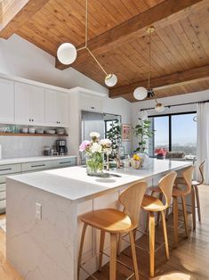 a kitchen with white counter tops and wooden ceilinging, along with bar stools