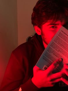 a man reading a book with red light coming from his face and hands over his mouth