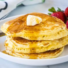 stack of pancakes with butter and strawberries on the side