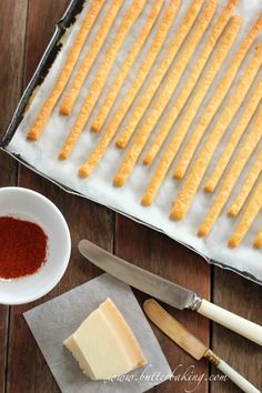 cheese sticks are lined up on top of parchment paper and next to a bowl of red seasoning