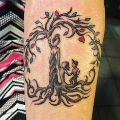 a person with a tattoo on their arm holding a child's hand while standing in front of a tree