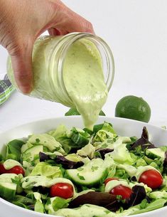 someone pouring dressing into a salad in a white bowl with lettuce, tomatoes and cucumbers