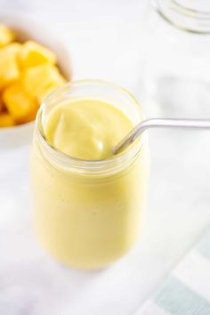 a glass jar filled with yellow liquid next to sliced pineapples and a spoon