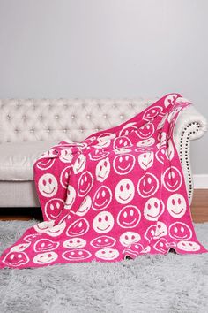 a pink blanket sitting on top of a white couch next to a white chair and rug