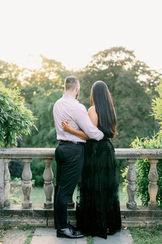 an engaged couple standing on a balcony looking at the trees