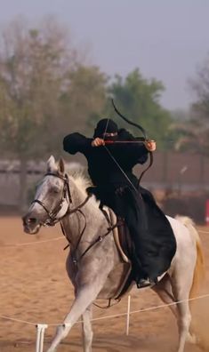 a man riding on the back of a white horse while holding a bow and arrow