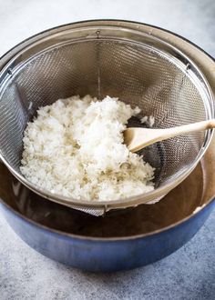 rice is being cooked in a strainer with a wooden spoon on the side,