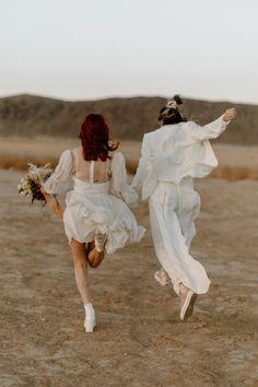 two women in white dresses are running through the desert