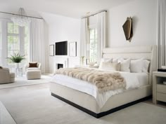 a large white bed sitting inside of a bedroom next to a chair and window covered in fur