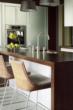 a kitchen island with two chairs and a bowl of fruit on the counter next to it