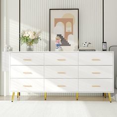 a white dresser sitting next to a wall with pictures on it and flowers in vases