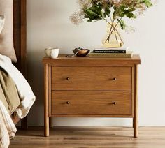 a nightstand with flowers on it next to a bed