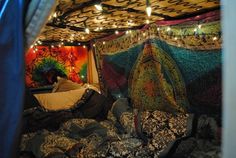 a bed covered in lots of blankets and pillows with lights strung from the ceiling above it