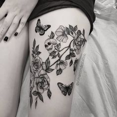 a woman's thigh with flowers and butterflies on her thighs, while the leg is covered in black ink