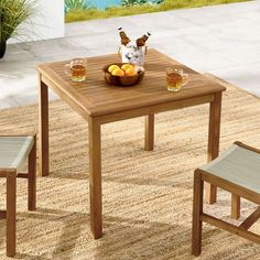 an outdoor table with two chairs and a bowl of fruit on it, in front of a pool