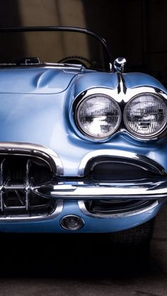 the front end of an old fashioned blue car with chrome grilles and headlamps