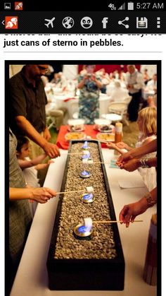 people standing around a long table with candles on it and one person lighting the candles