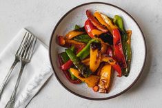 a white plate topped with stir fry vegetables next to a fork and napkin on top of a table