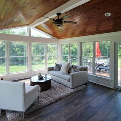 a living room filled with white furniture and lots of windows next to a wooden ceiling