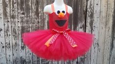 a red and pink tutu skirt with an orange face on it, sitting in front of a wooden fence