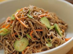 a white bowl filled with noodles and veggies on top of a wooden table