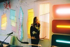 a woman standing next to a bike in front of a wall with colorful lights on it