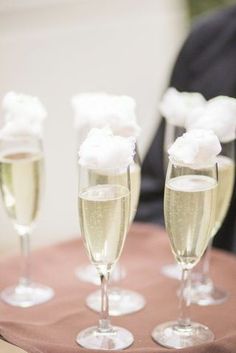 three champagne flutes are sitting on a table with white flowers in the middle and one is filled with bubbles