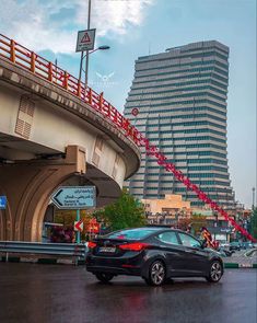 a black car driving down a wet street next to tall buildings in the background with red tape on it