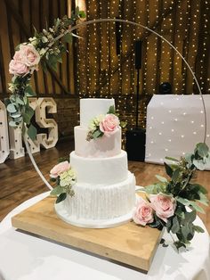 a three tiered wedding cake with pink flowers on the side and greenery around it