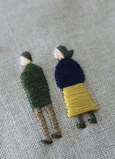 two small embroidered dolls sitting next to each other on a piece of cloth with thread