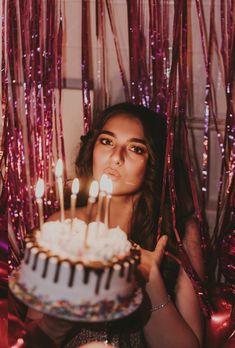 a woman holding a cake with lit candles in front of her face and pink streamers behind her