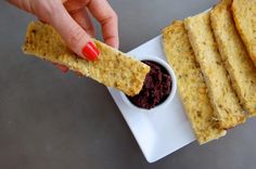 a person dipping something into a small bowl with some sort of cracker on it