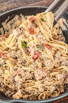 a skillet filled with pasta and meatballs on top of a wooden table next to a fork