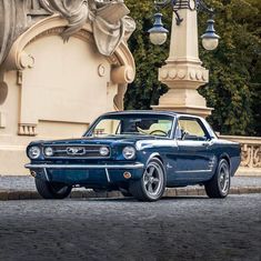 an old blue car parked in front of a statue