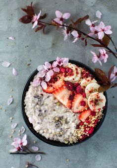 a bowl filled with oatmeal topped with sliced bananas and strawberries next to pink flowers