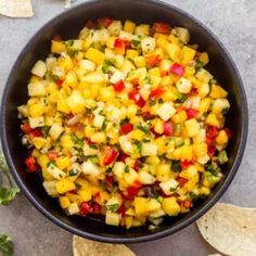 a black bowl filled with pineapple salsa surrounded by tortilla chips and cilantro