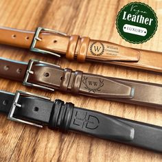 three leather belts on a wooden table with a green label over it that says leather luxury