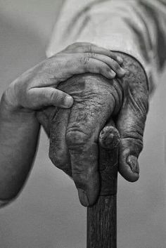 an old person holding the hand of another person on top of a wooden pole in black and white