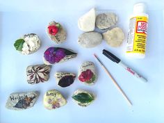 some rocks with flowers and leaves painted on them next to paintbrushes, glue and markers