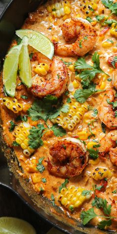 a skillet with shrimp, corn and cilantro on it next to lime wedges