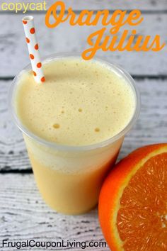 an orange smoothie in a plastic cup next to an orange on a wooden table