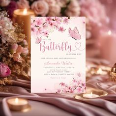 a pink and white butterfly themed wedding card on a table with candles, flowers and other decorations