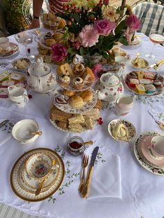 a table topped with lots of plates and cups filled with food next to a vase full of flowers