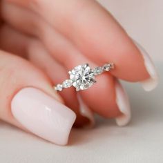 a woman's hand holding a diamond ring on her left hand with white nails