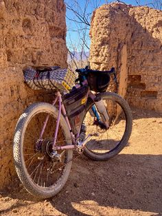 a pink bike parked next to a stone wall with a backpack on it's back