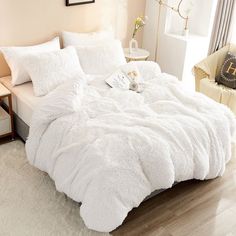 a bed with white comforter and pillows in a room next to a chair on the floor