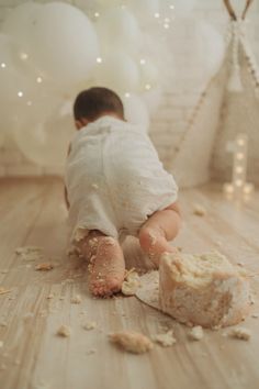 a baby crawling on the floor next to a cake