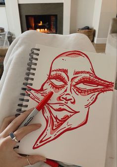 a person is drawing on paper with a red marker and pen in front of a fire place